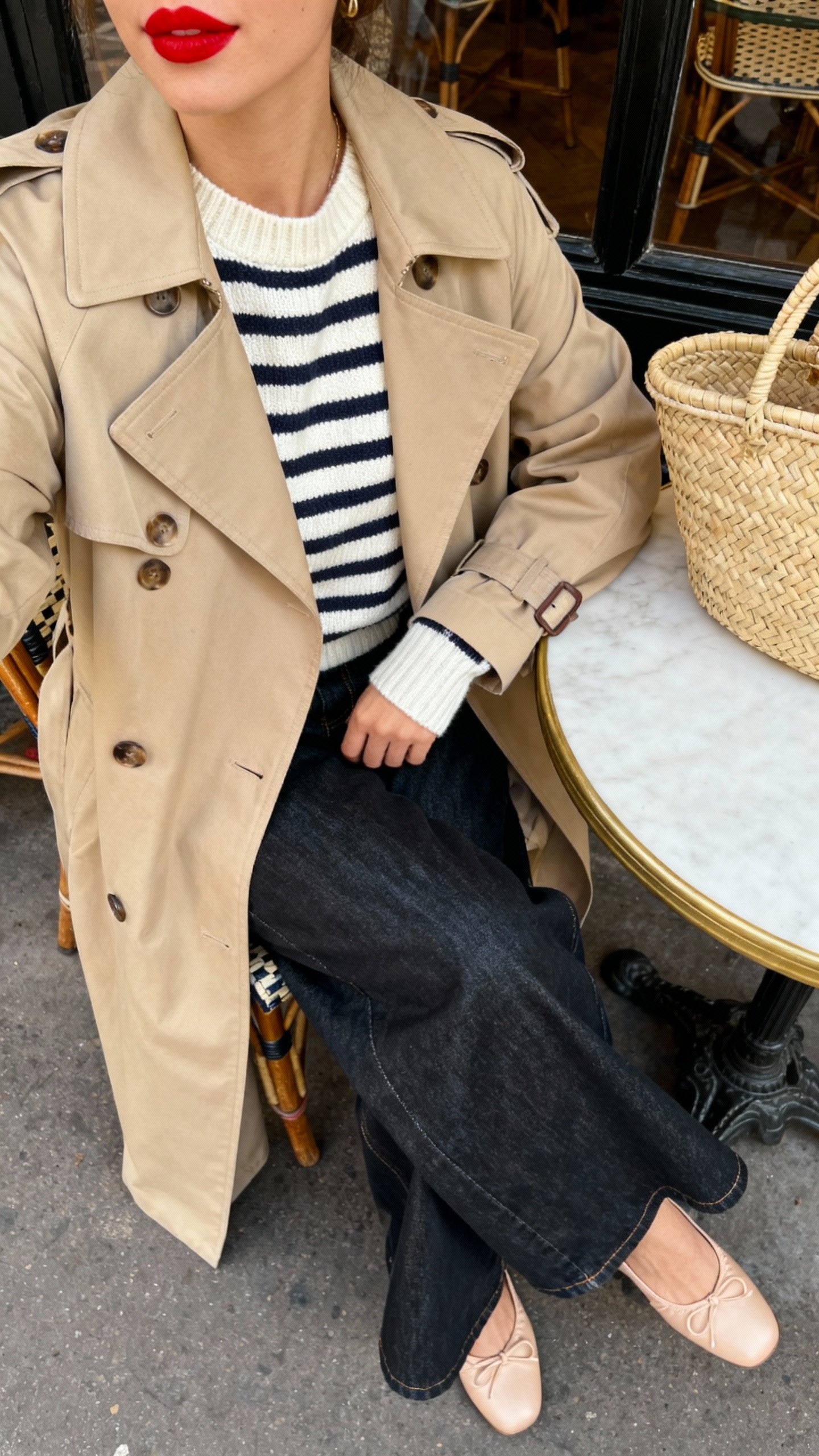 iPhone cafe table selfie cropped at shoulders showing a Breton striped knit under a beige trench, wide-leg dark denim, ballet flats, red lip peeking off-frame, woven tote, face not visible, Parisian-style cafe setting, soft daylight, natural iPhone quality.