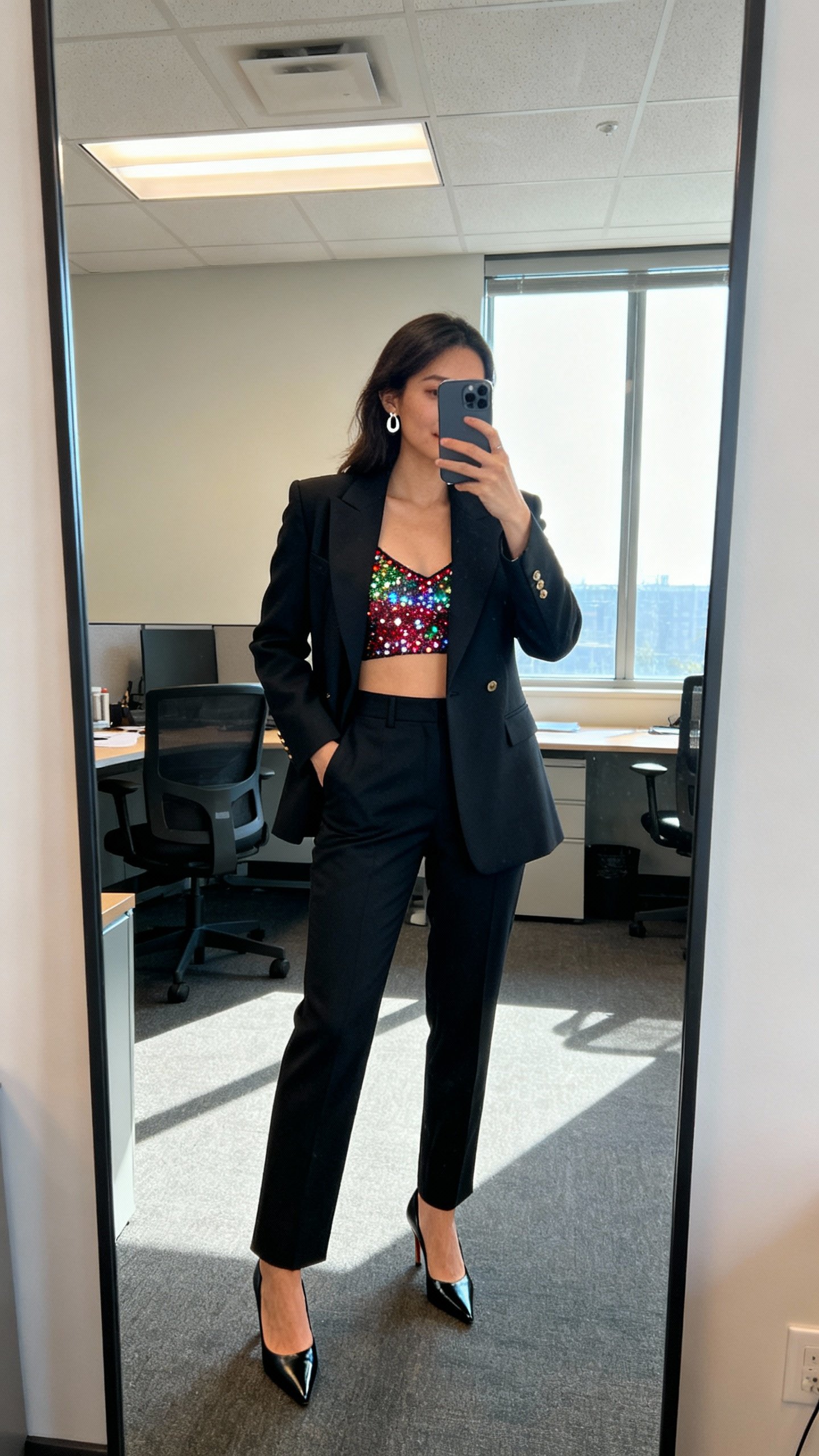 iPhone office mirror selfie of a tailored power suit with a festive twist (sparkly cami under the blazer), pointed heels, subtle earrings, face not visible, fluorescent office lighting mixed with window light, natural iPhone photo.