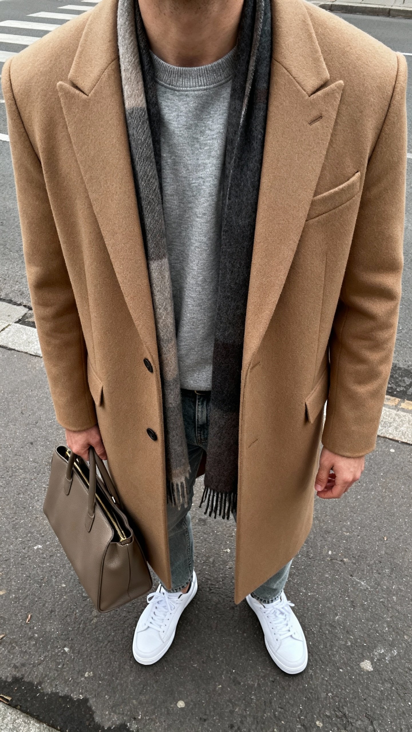 iPhone street selfie, neck-down, showing classic grey crewneck under camel tailored coat with relaxed jeans and clean white sneakers, scarf and structured tote, face not visible, overcast daylight, natural iPhone photo.