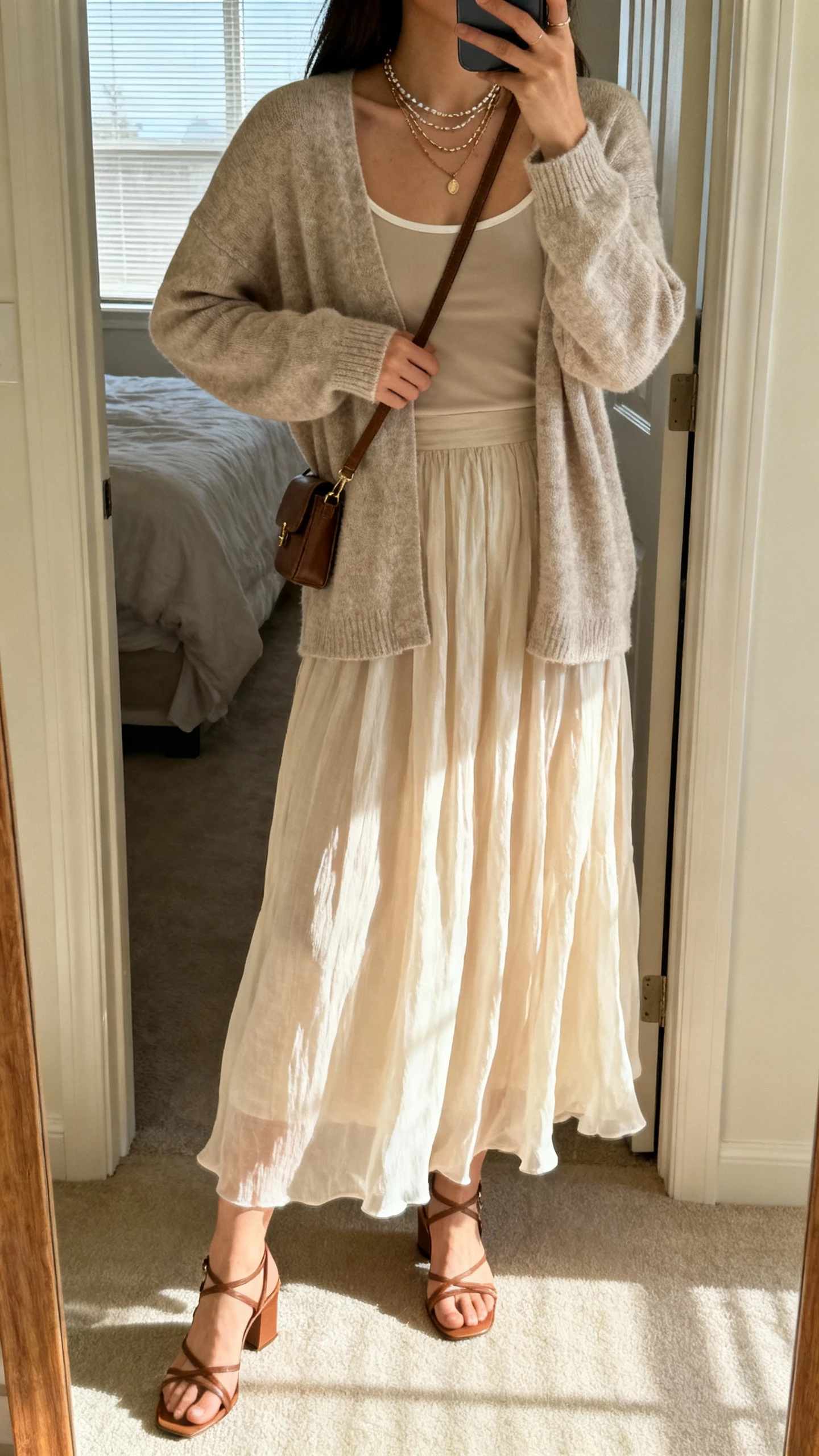iPhone back-view selfie of a woman wearing a soft cardigan over a camisole and a floaty maxi skirt, strappy low heels, layered necklaces, small crossbody, face not visible, bedroom doorway mirror, afternoon window light, natural iPhone photo quality.