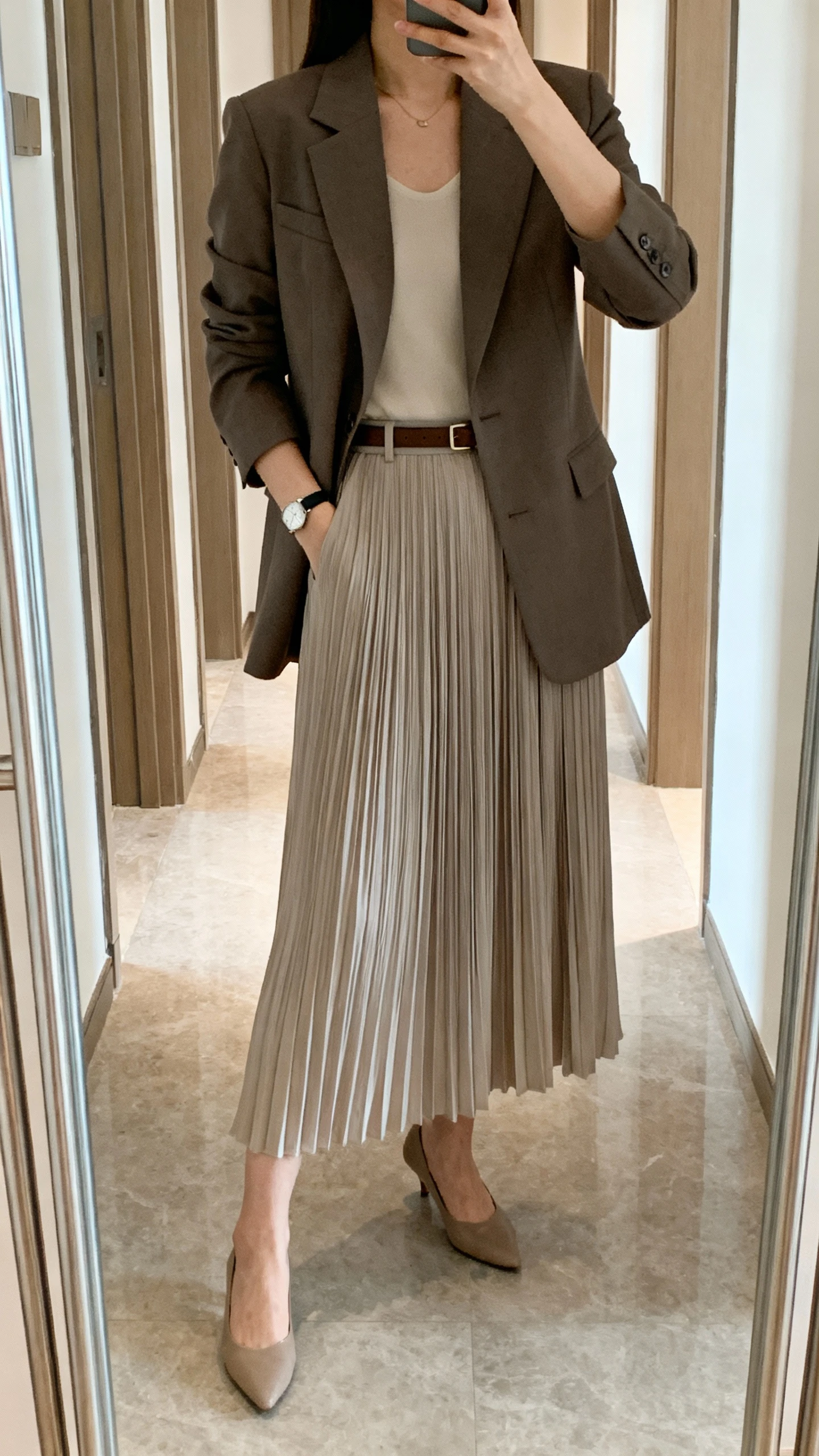 iPhone mirror selfie of a woman in a tailored blazer over a pleated midi skirt with a slim belt, low heels, simple watch, face not visible, hallway full-length mirror, soft indoor daylight, natural iPhone aesthetic.