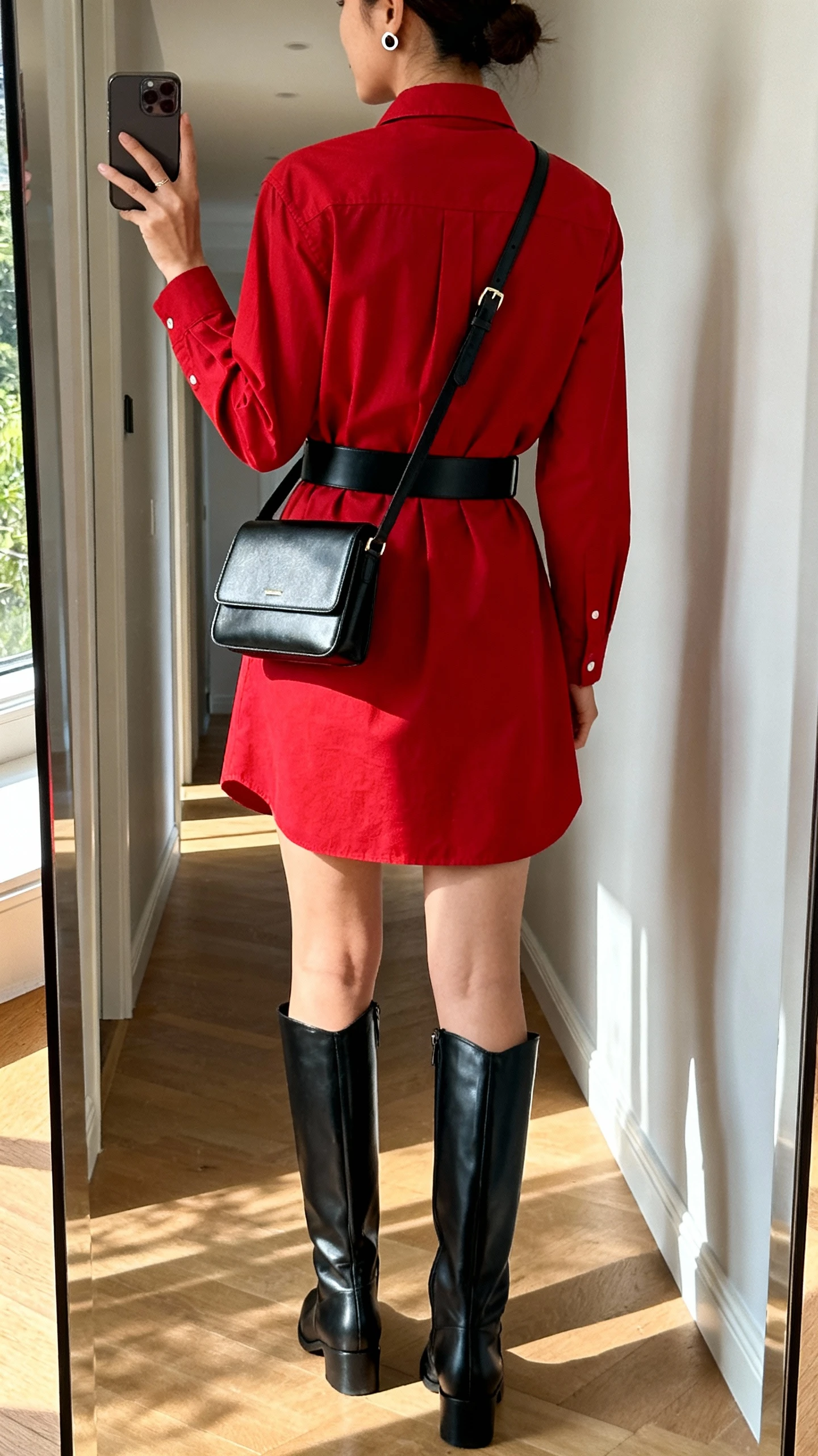 iPhone back-view mirror selfie of a woman wearing a belted red shirt dress with tall black leather boots, black waist belt, structured crossbody, simple stud earrings, face not visible, hallway mirror, natural afternoon light, iPhone photo quality