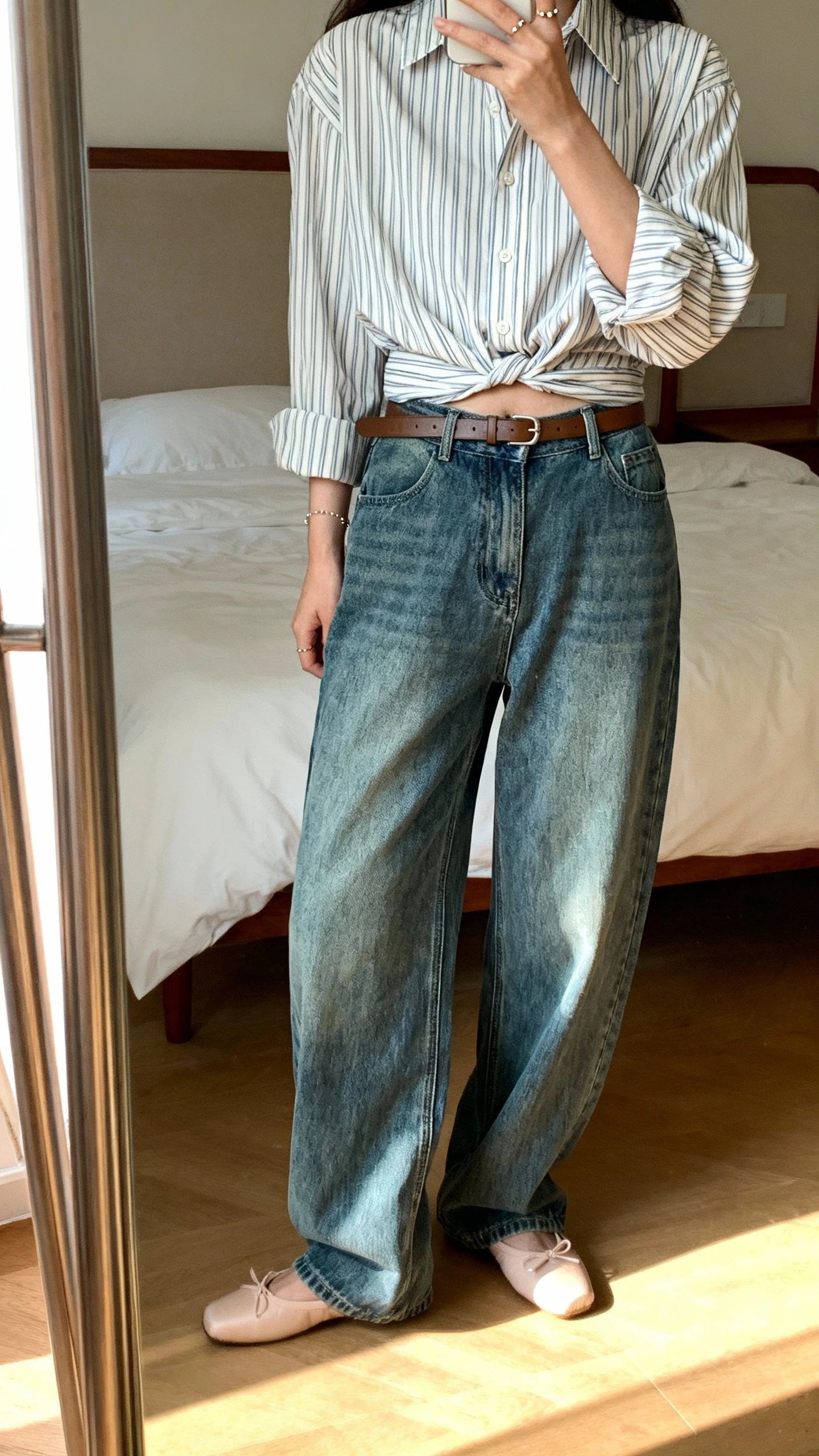 iPhone back view of a woman wearing baggy jeans with a French-girl striped button-down half-tucked, ballet flats, slim leather belt, dainty studs, face not visible, bedroom mirror, soft afternoon light, iPhone photo quality.