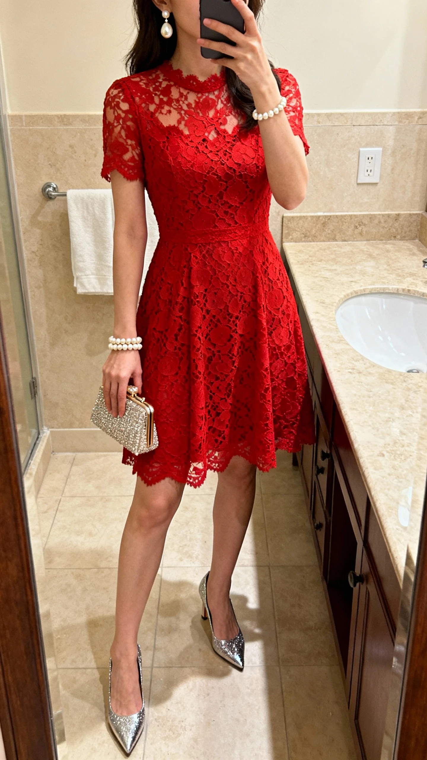 iPhone mirror selfie of a woman wearing a red lace cocktail dress, pearl drop earrings, pearl bracelet, sparkly metallic heels, miniature evening clutch, face not visible, bathroom mirror, warm indoor lighting, iPhone photo quality
