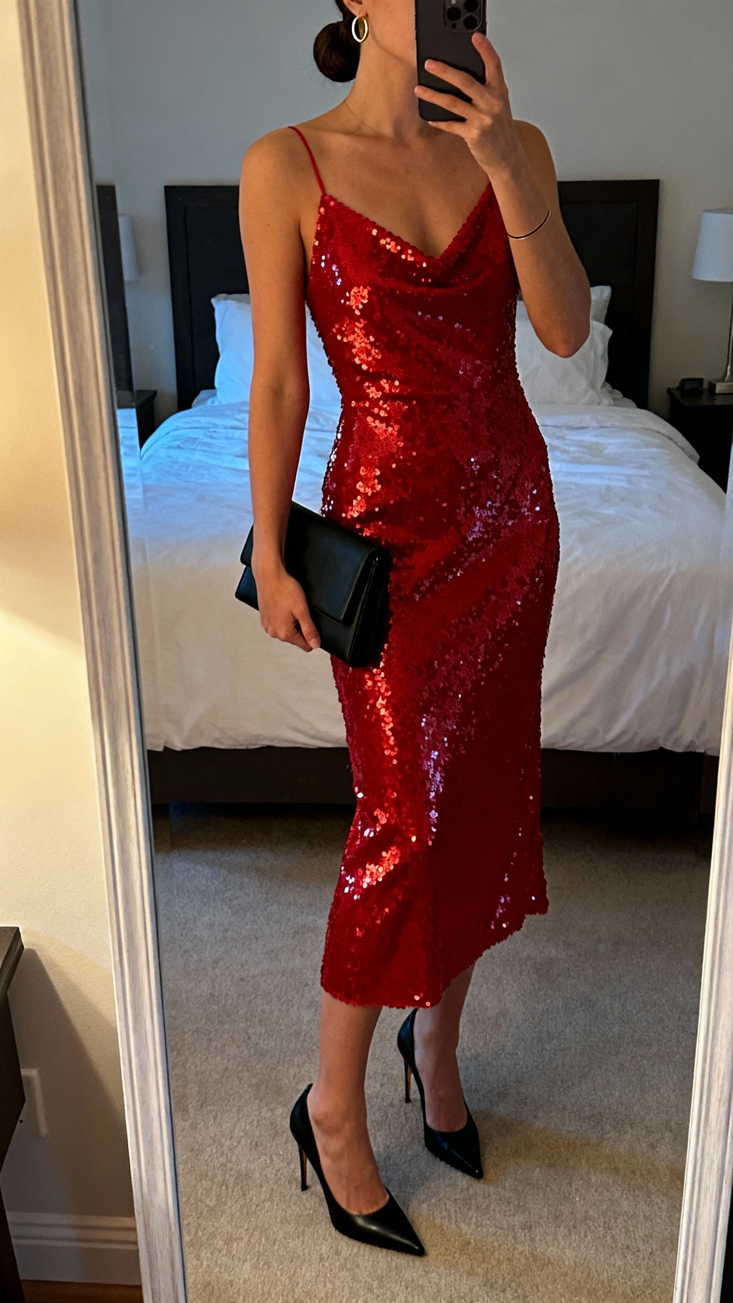 iPhone mirror selfie of a woman wearing a sequined red dress, sleek black stilettos, minimalist black clutch, thin gold hoops, smooth low bun, face not visible, cropped at shoulders, bedroom mirror, soft evening indoor light, iPhone photo quality