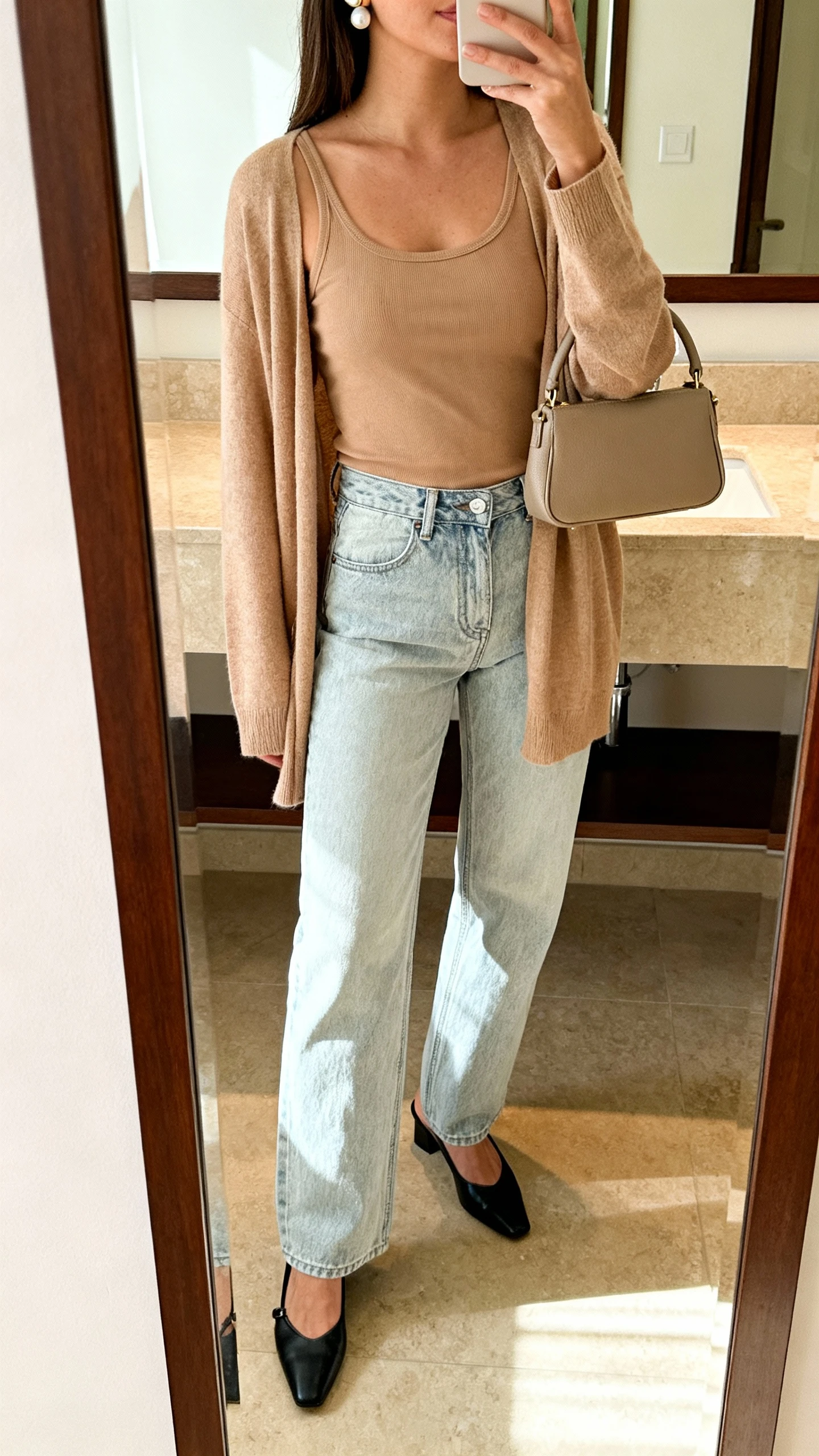 iPhone mirror selfie of a woman wearing light-wash mom jeans, a matching cardigan set (tank + cardigan) in soft tan, black slingback flats, pearl studs, and a small top-handle bag, face not visible, bathroom mirror, warm indoor lighting, iPhone photo quality.